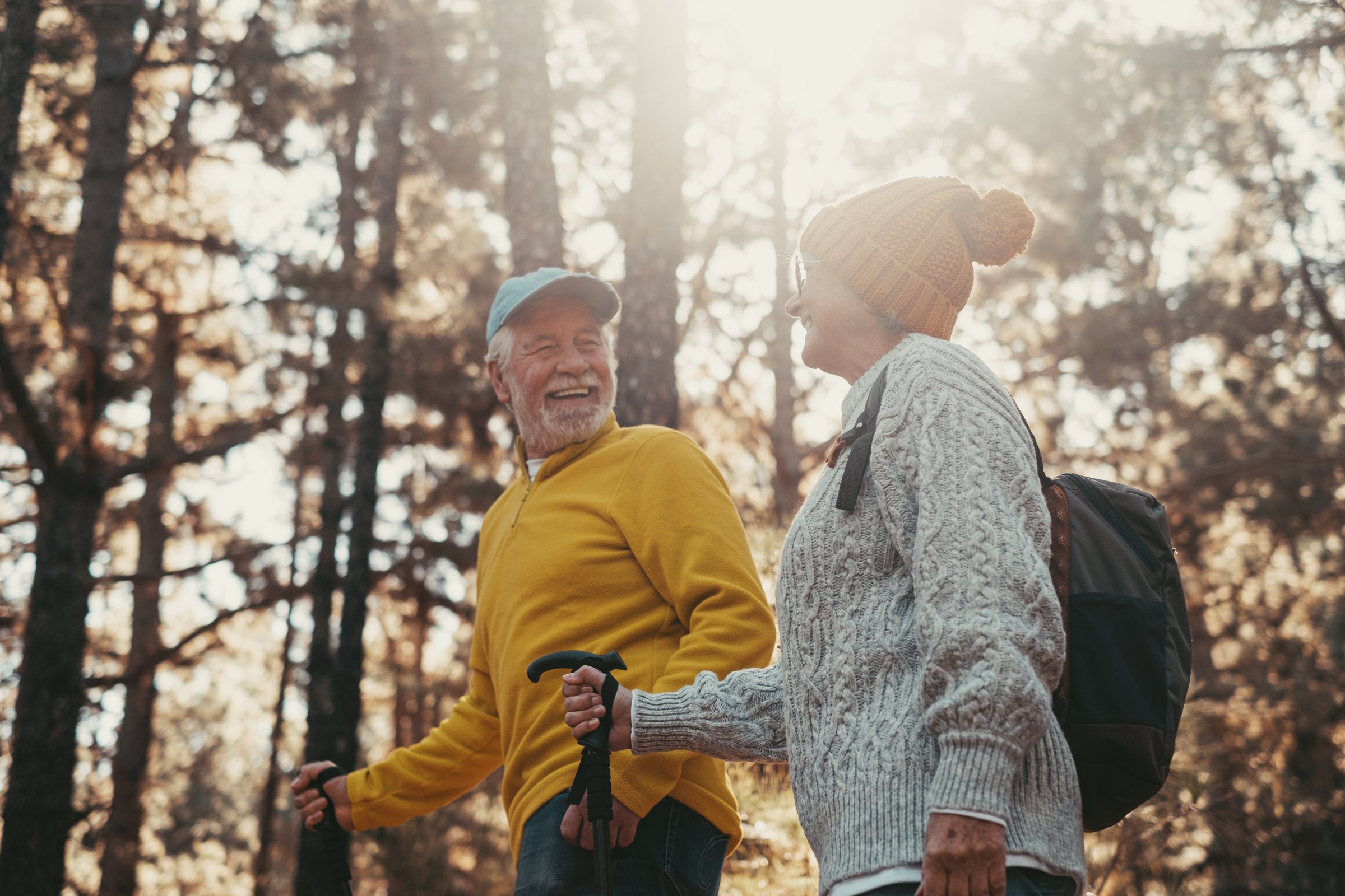 An older couple hiking together through a sunlit forest