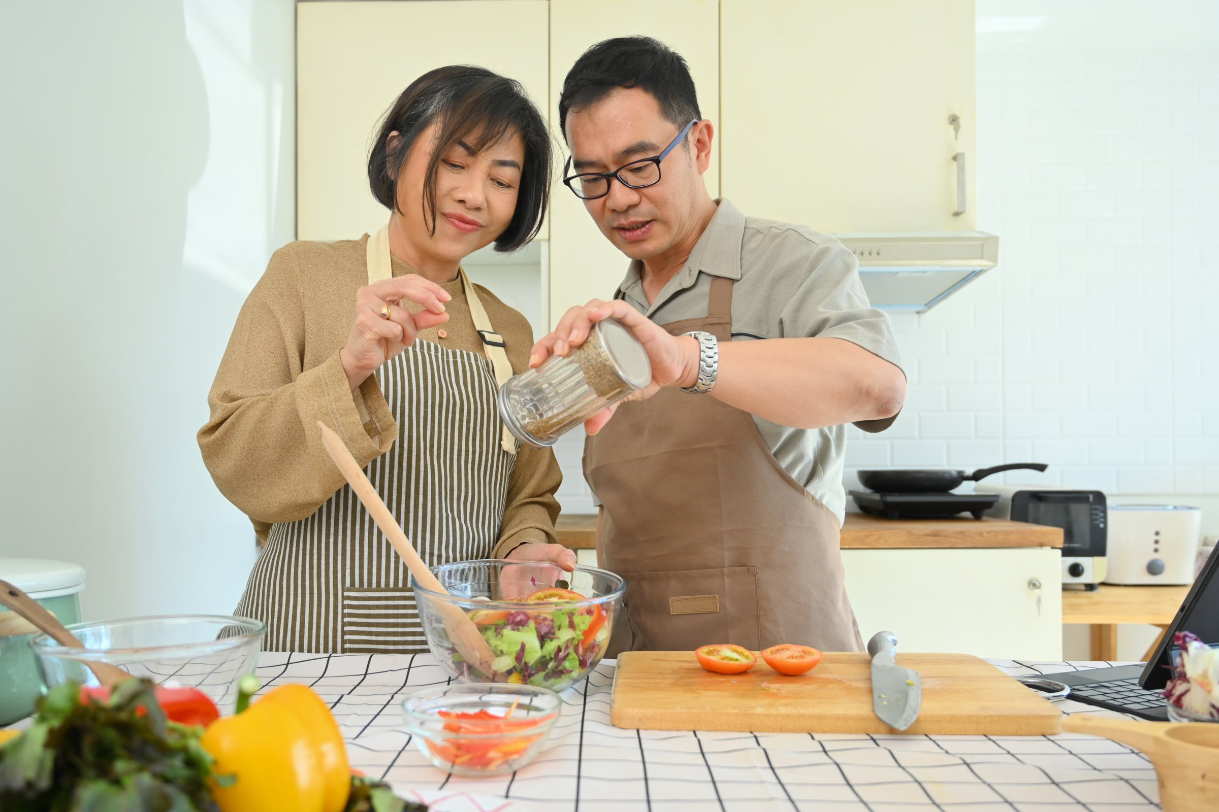 A middle-aged man and woman preparing a healthy salad at home