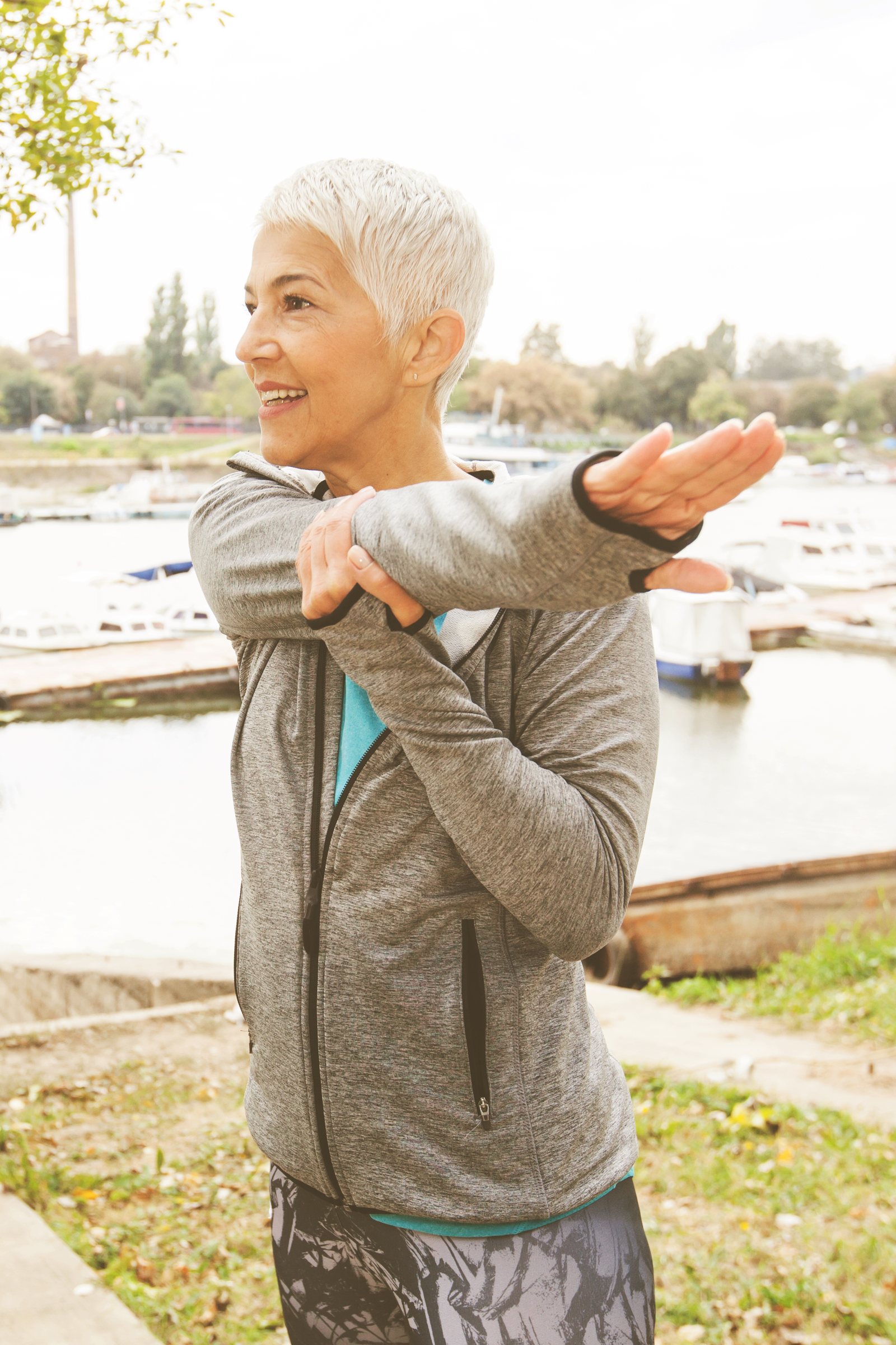 A mature woman stretching beside the water in soft daylight