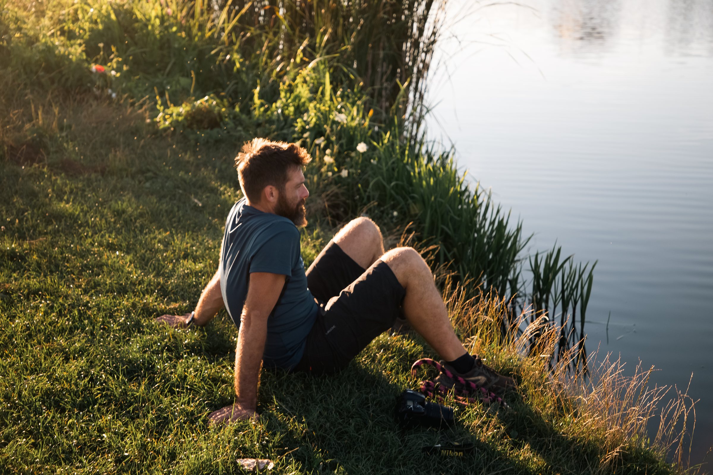 A man in his thirties relaxing beside a pond at sunset